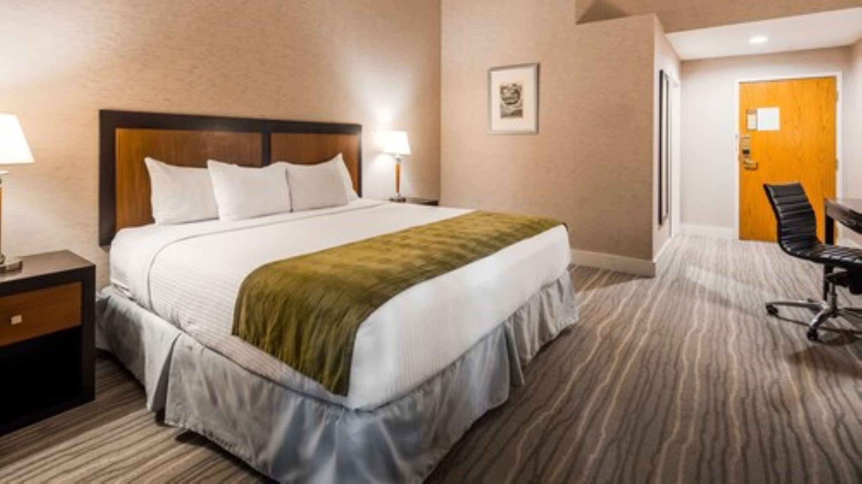 Een hotelkamer met een bed, een bureau, een stoel, een nachtkastje en een deur.