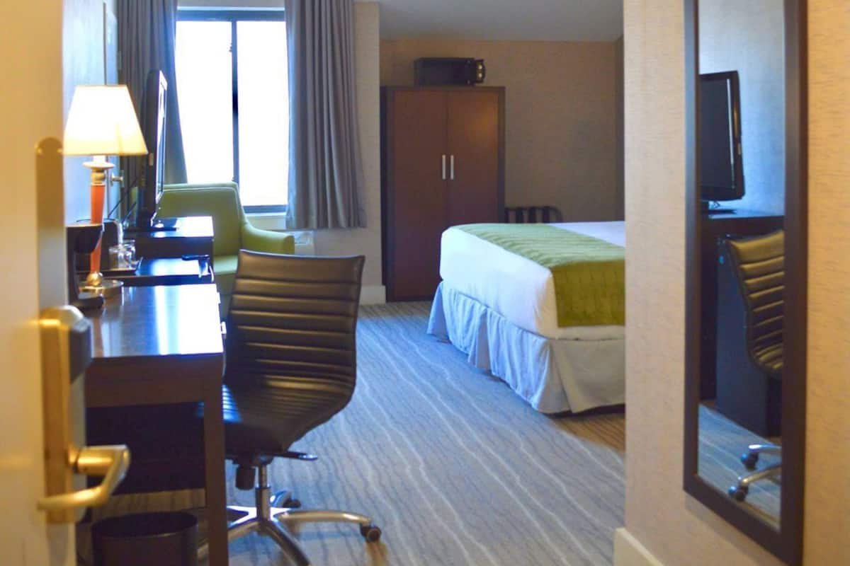 A hotel room with a desk, chair, bed, and a large mirror.
