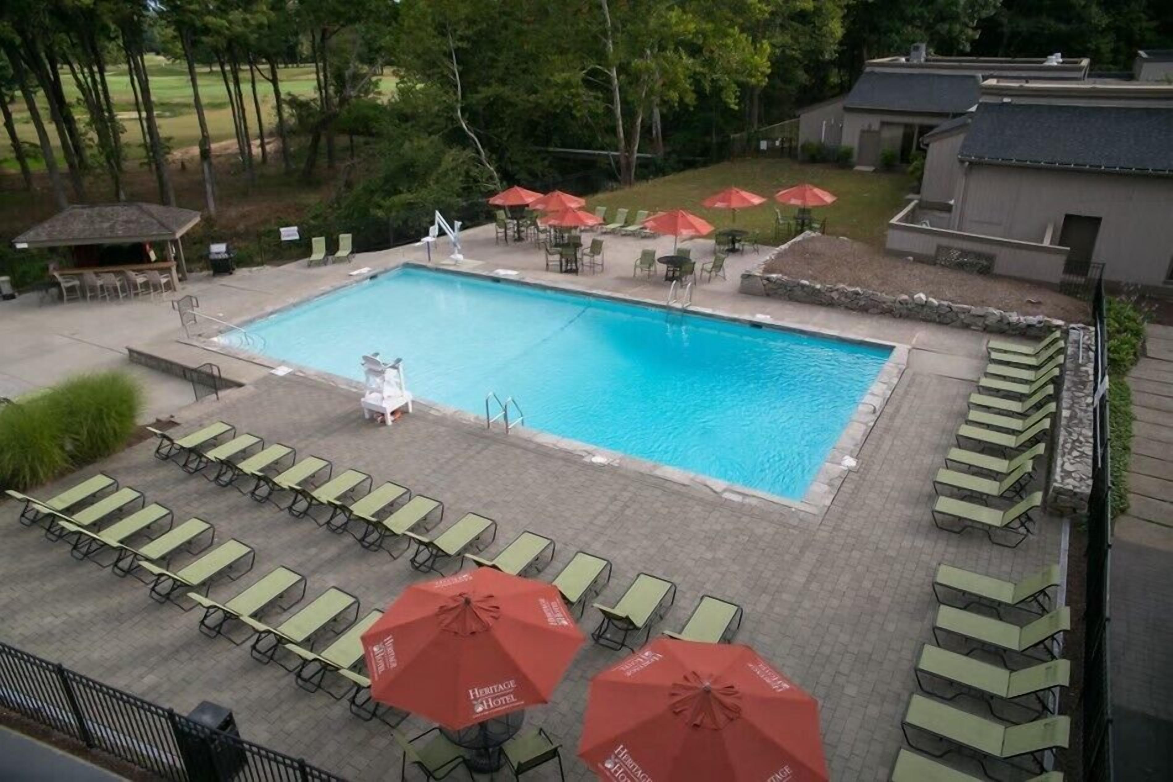 Una piscina rectangular rodeada de sillas de descanso y sombrillas rojas.