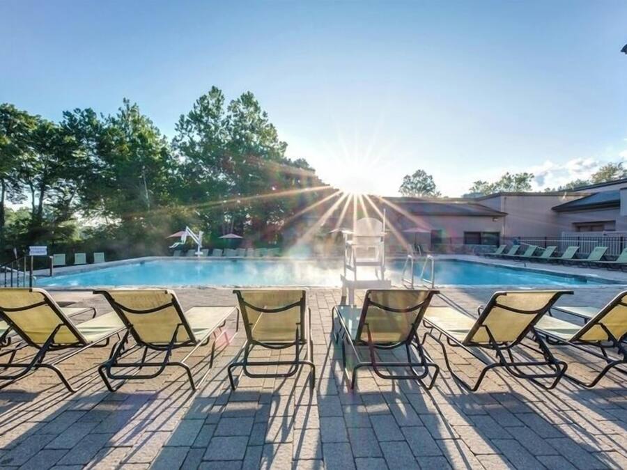 A pool area with sun rays, lounge chairs, and a building in the background.