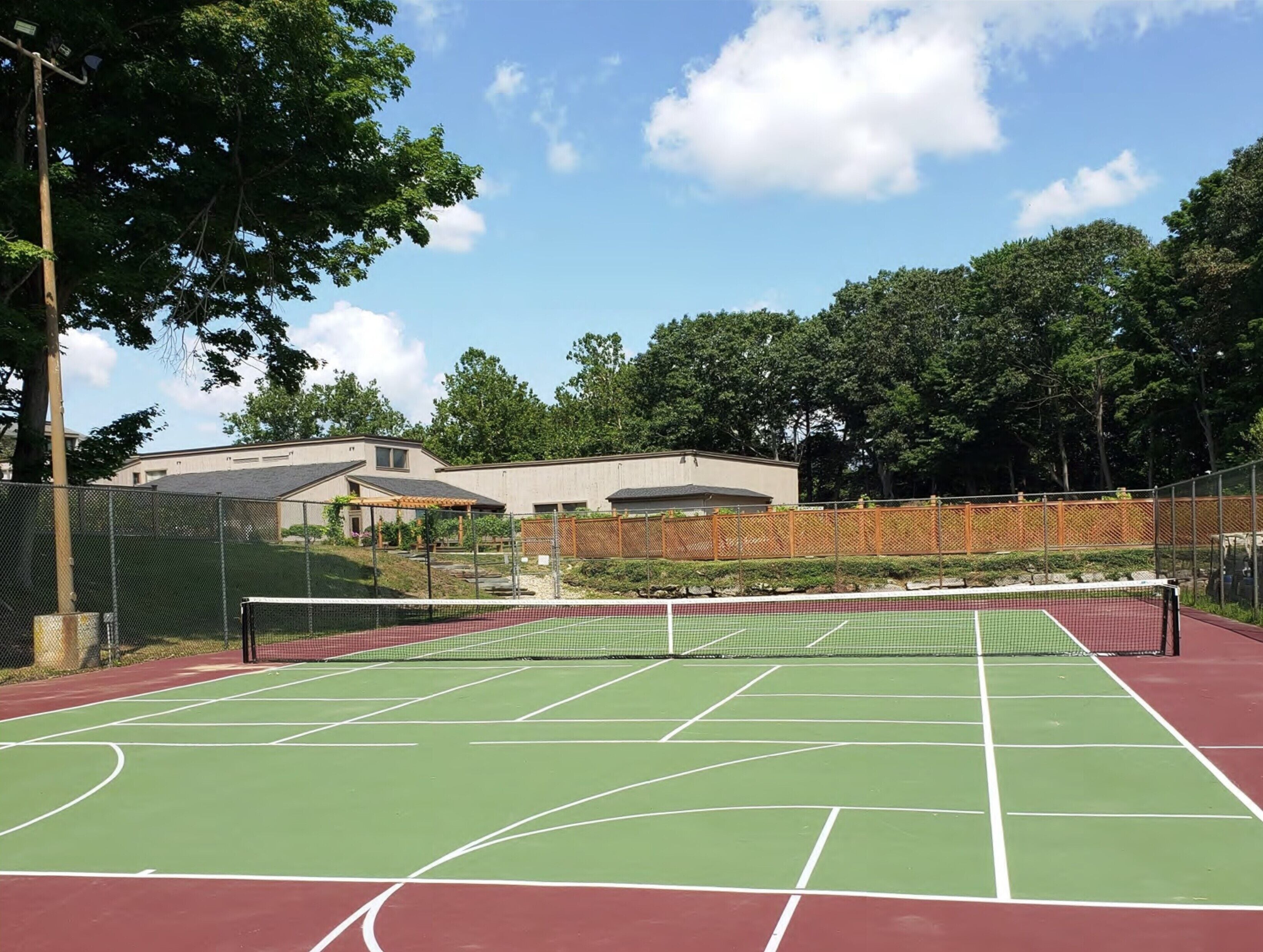 A tennis court with a net, surrounded by trees and a building in the background.