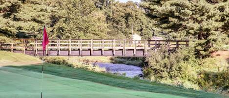 Un campo de golf con un puente de madera, una bandera y un estanque.