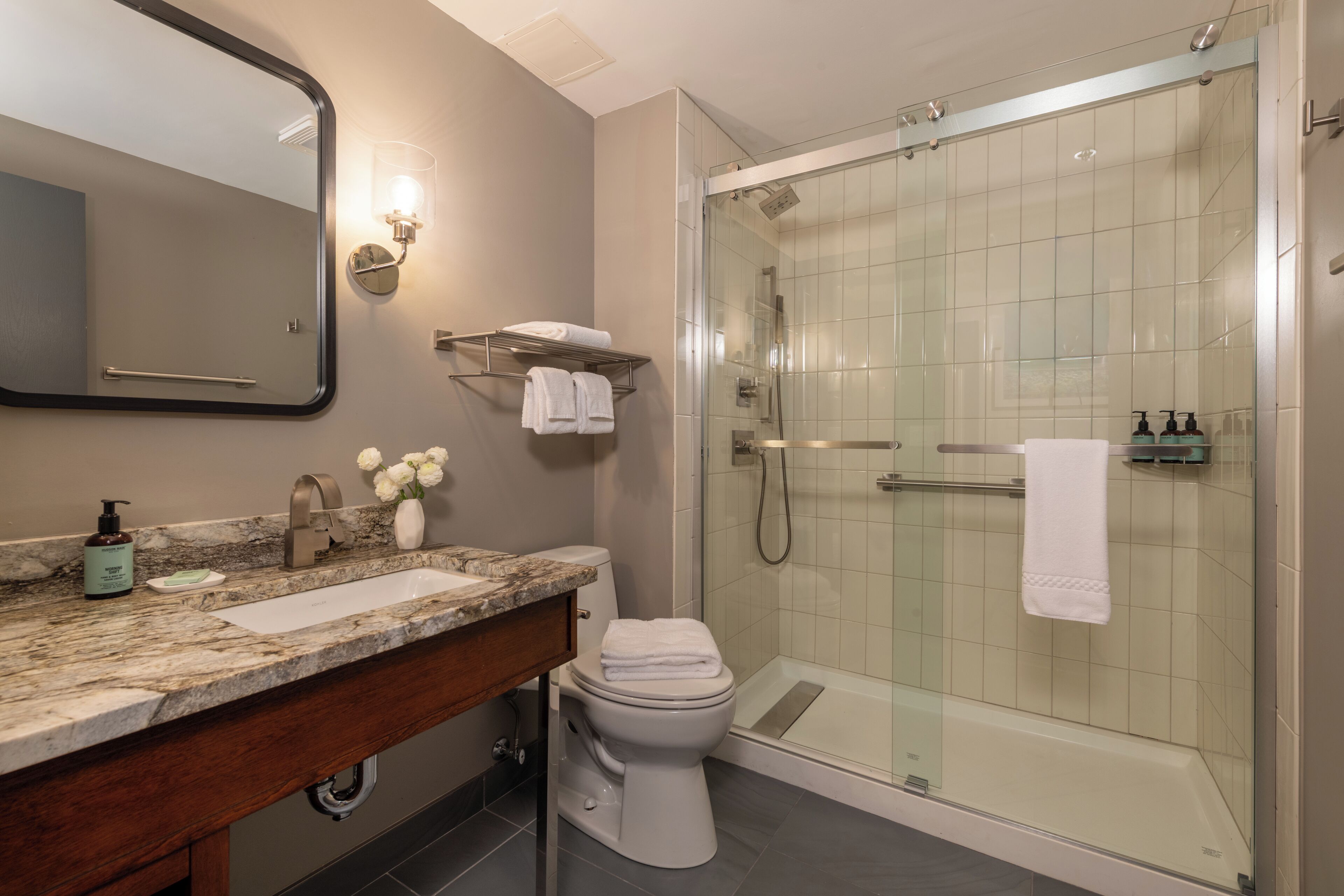 Een moderne badkamer met een douchecabine van glas, een marmeren wastafel en een toilet.