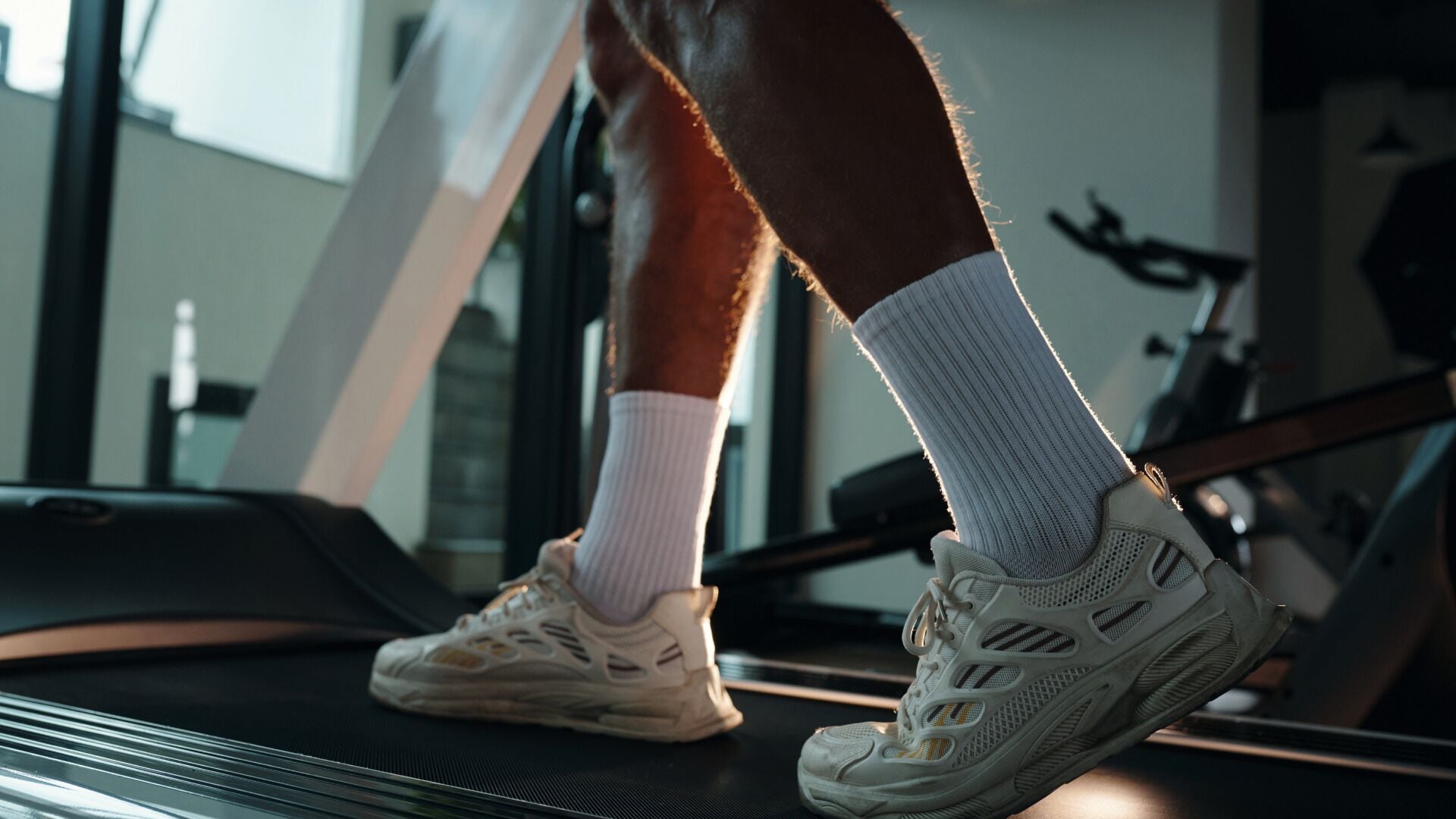 Une personne court sur un tapis de course dans une salle de sport, avec du matériel d’exercice en arrière-plan.
