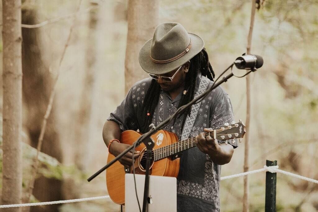 A person playing an acoustic guitar outdoors, with a microphone stand in front.