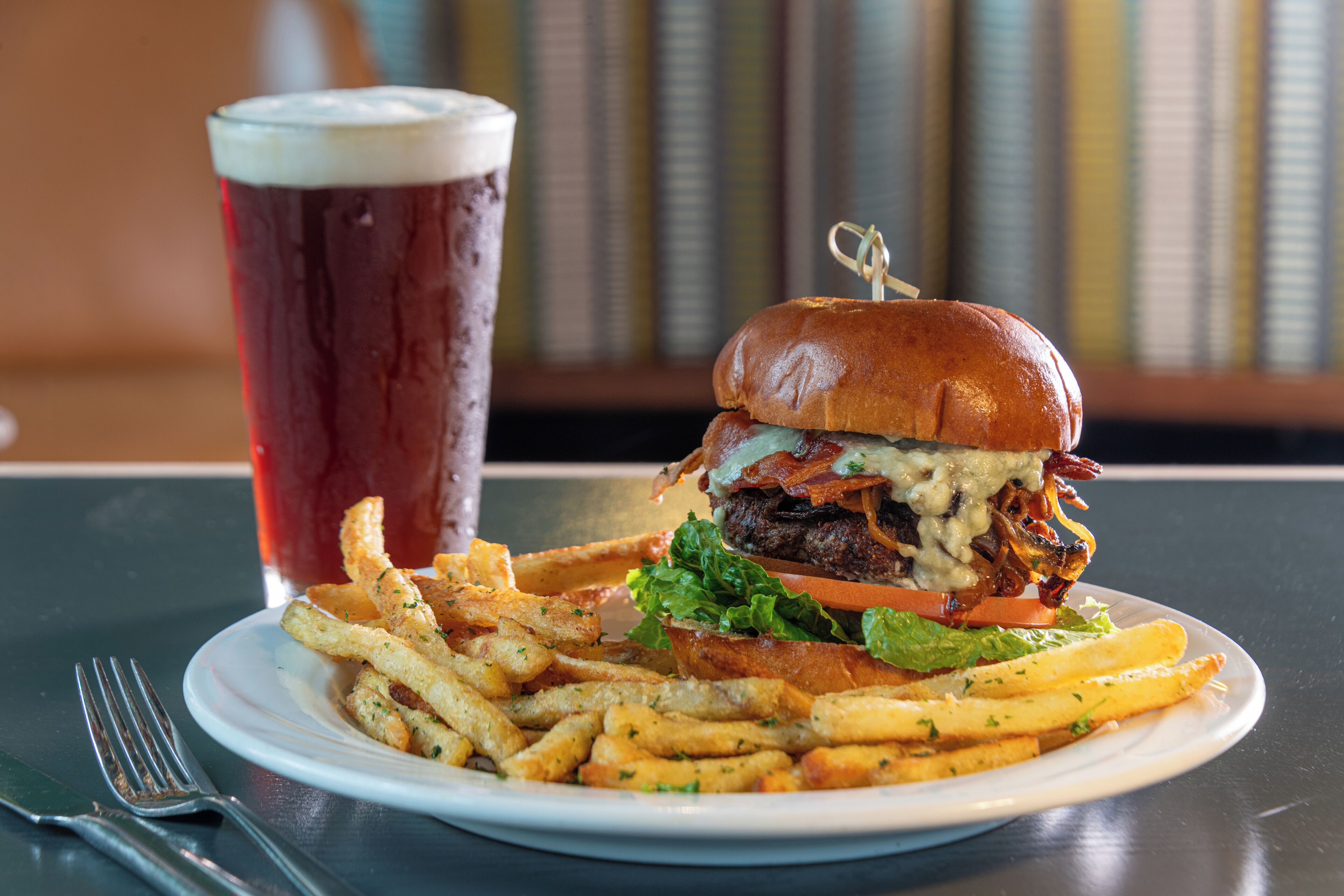 A burger with fries and a glass of beer on a table.