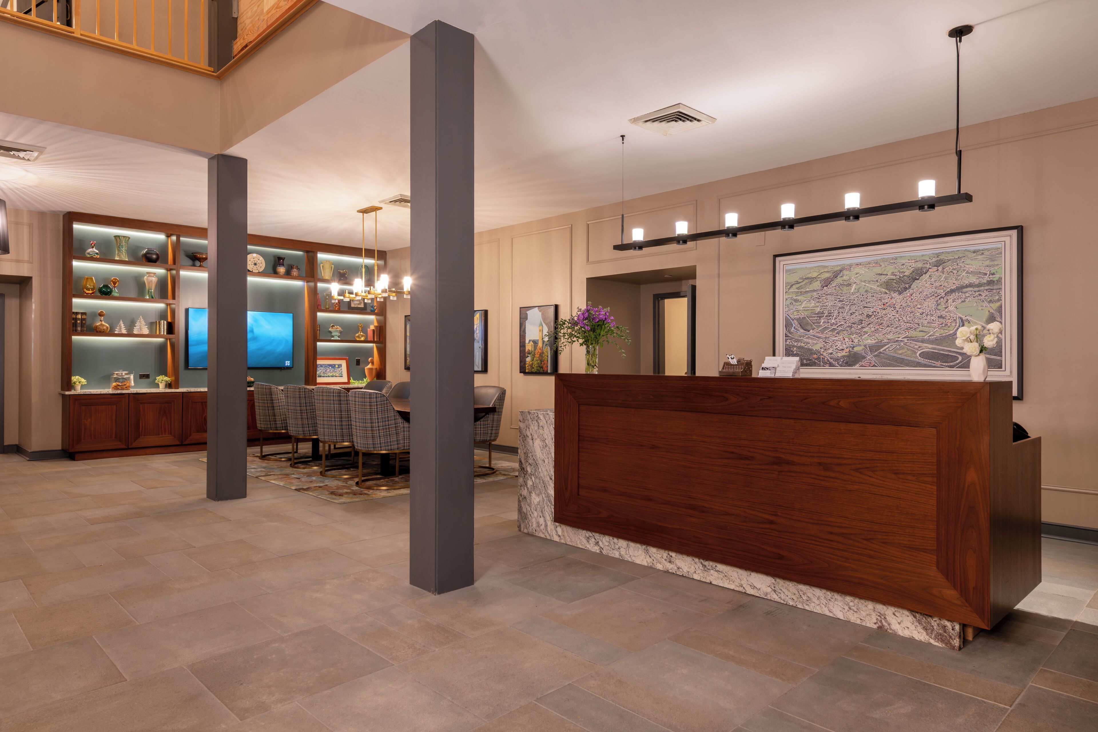 A spacious lobby with a reception desk, a dining area with a large table and chairs, and a wall with shelves displaying various items.