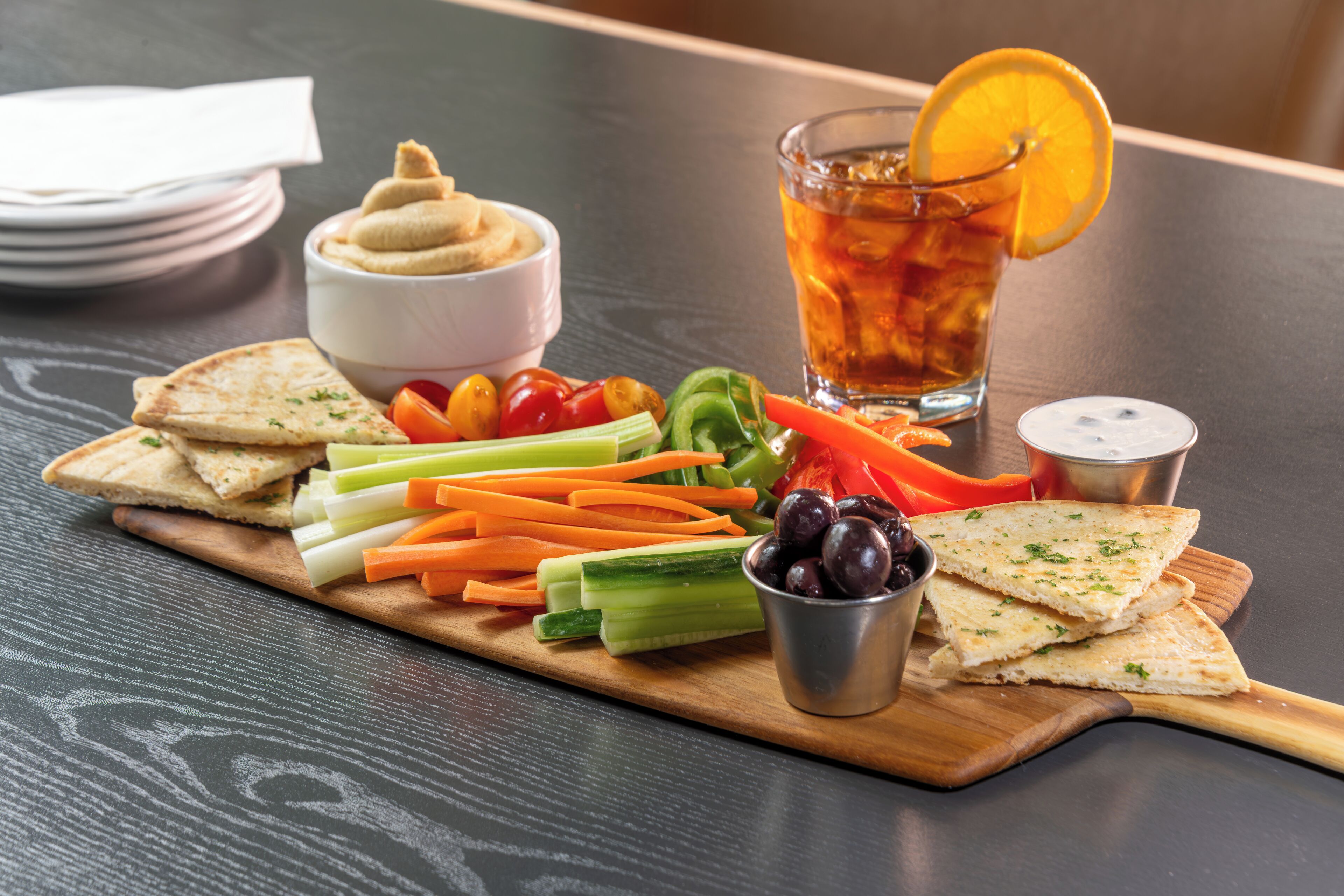A wooden board with various snacks and a glass of iced tea on a table.