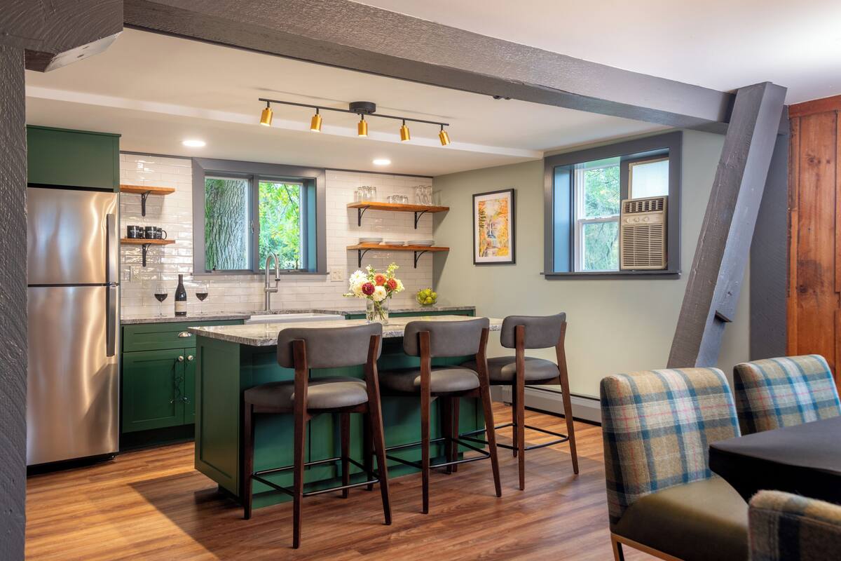 A modern kitchen with green cabinets, a stainless steel refrigerator, and a bar area with stools.