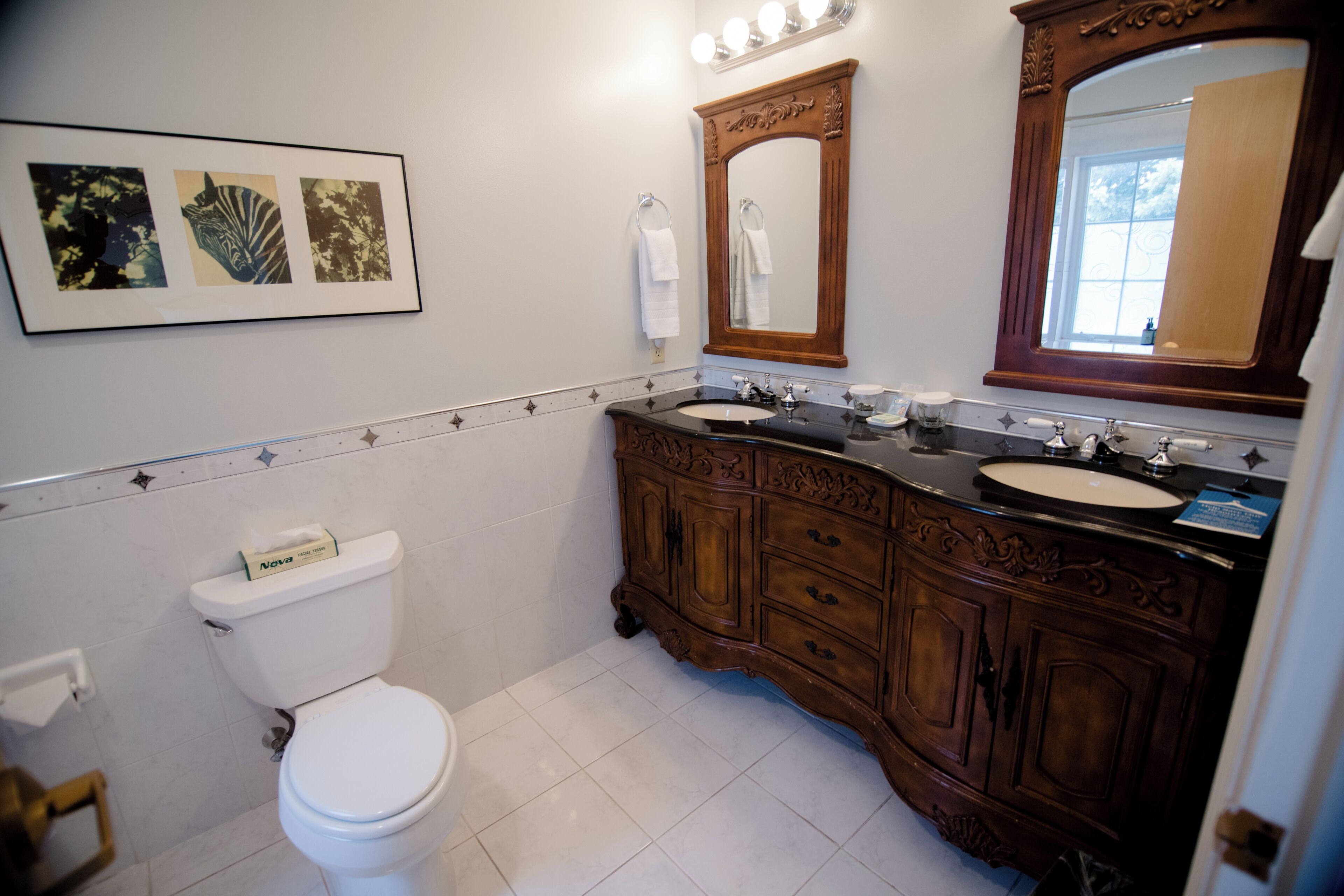 Une salle de bain avec des toilettes blanches, un meuble-lavabo en bois et un grand miroir au-dessus du meuble-lavabo.