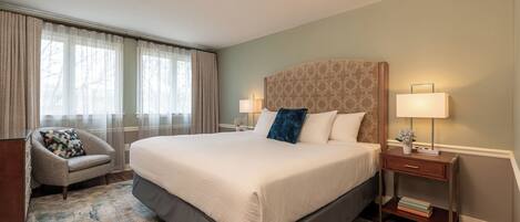 A neatly arranged hotel room with a large bed, a chair, a nightstand, and a window with curtains.