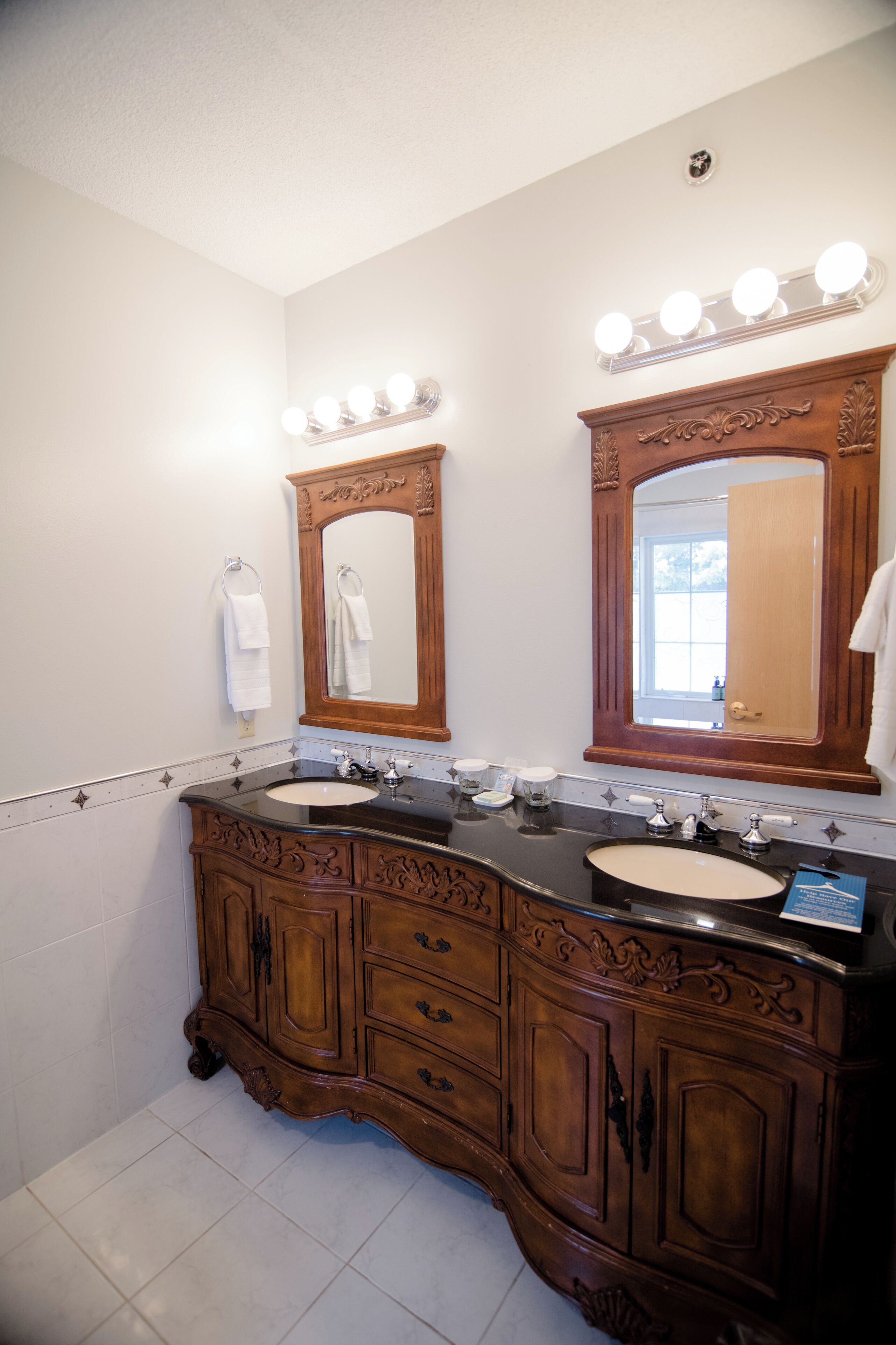 A bathroom with two sinks, a large mirror with lights, and a wooden vanity.