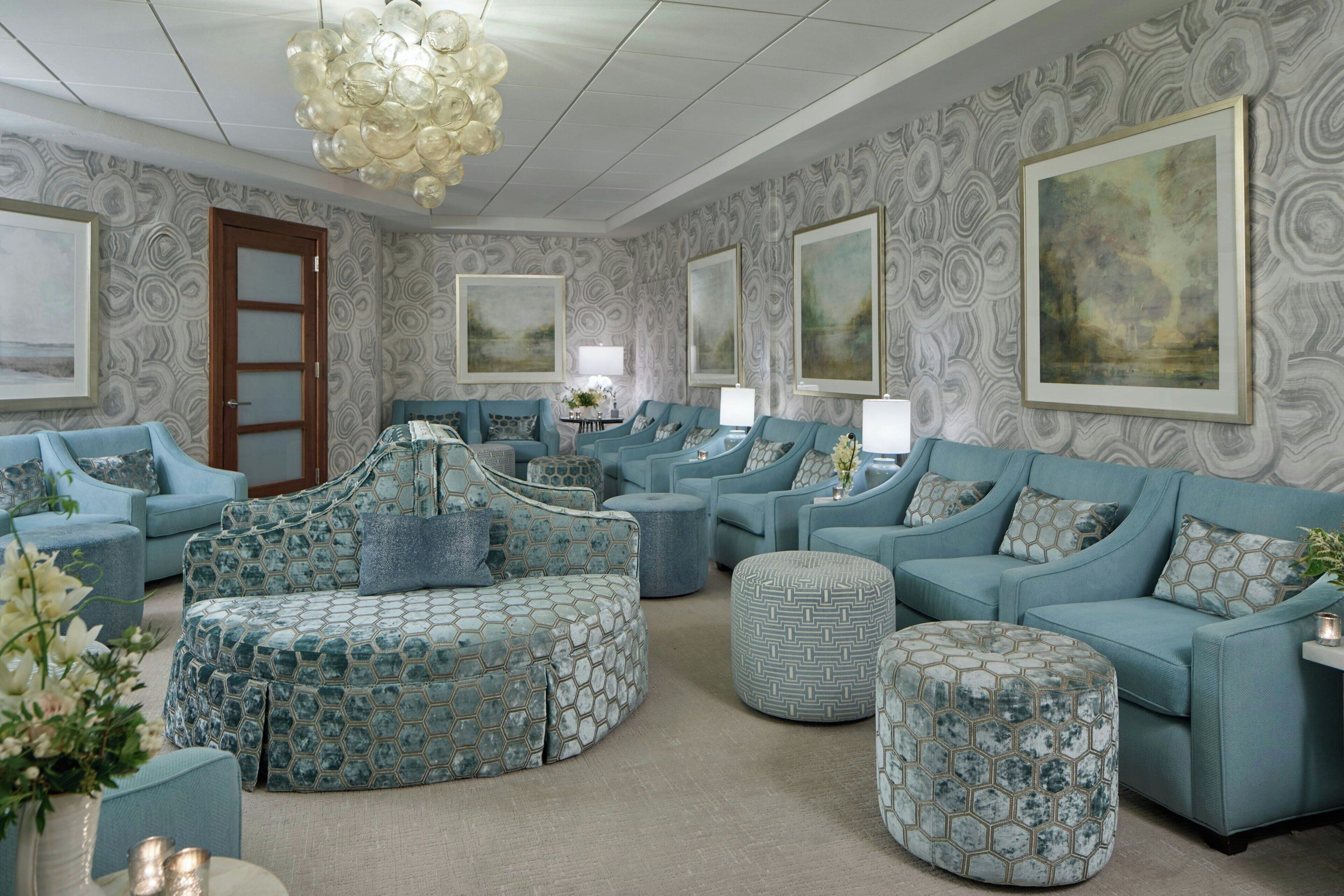 A spacious living room with a circular sofa, multiple ottomans, and a chandelier.