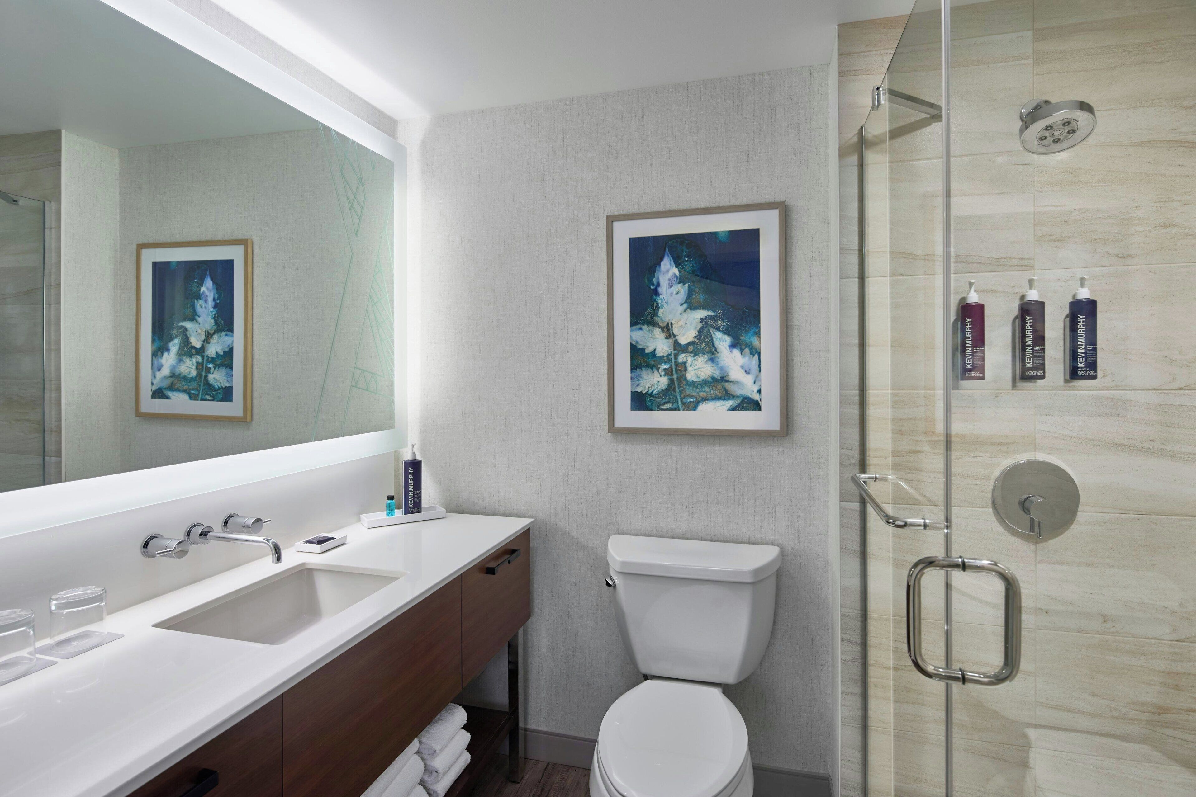 A bathroom with a large mirror, two sinks, a toilet, and a shower.
