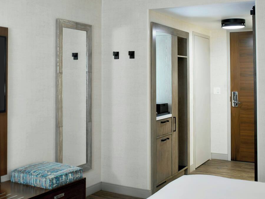 A hotel room with a bed, a wardrobe, a mirror, a television, and a small bedside table.