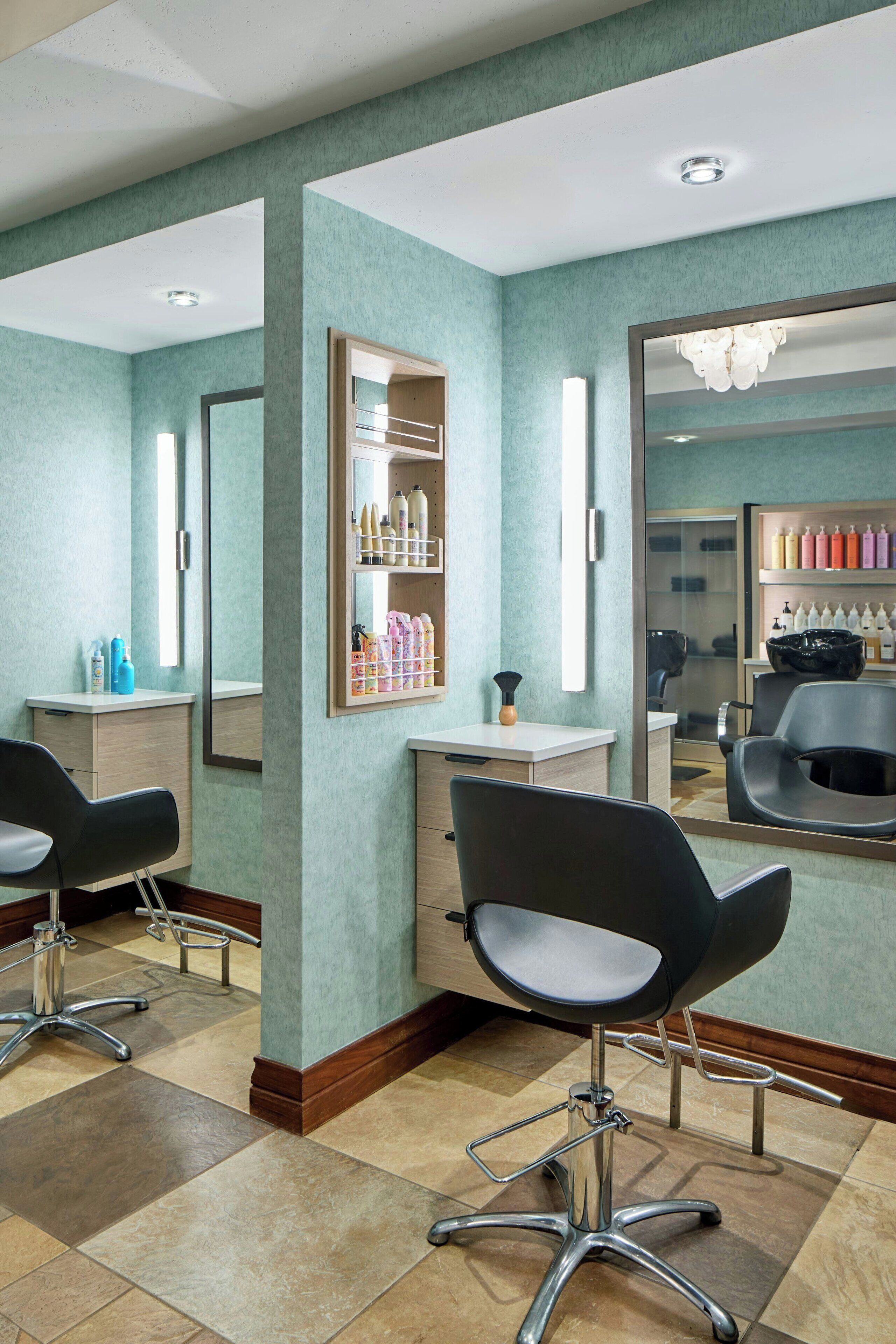 A salon with a teal wall, a mirror, a sink, and two chairs.