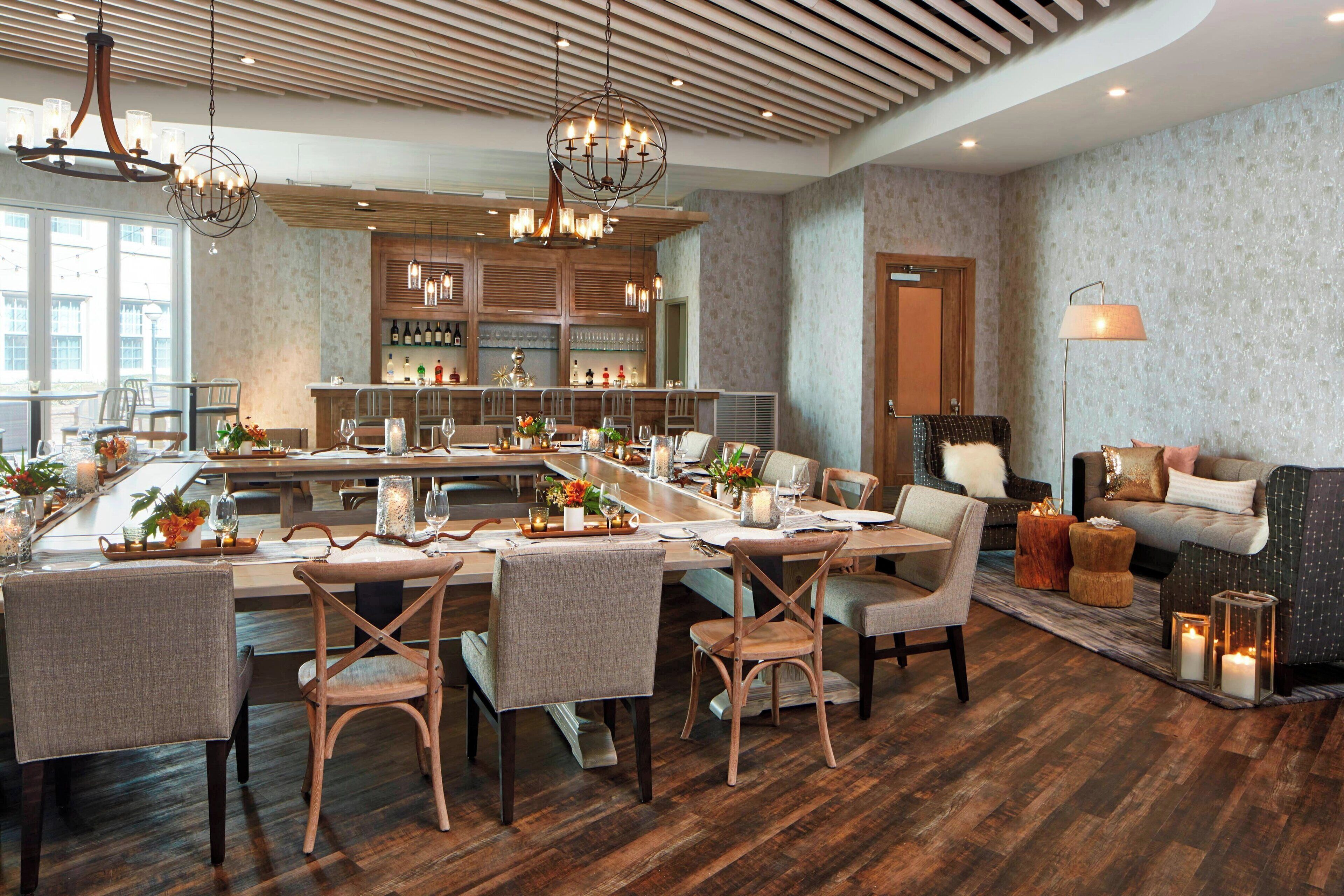 A spacious dining area with a long table, multiple chairs, and a bar area with shelves of bottles.