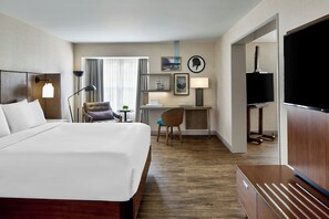 A hotel room with a bed, desk, chair, TV, lamp, and artwork on the walls.