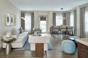 A modern living room with a sofa, ottoman, side table, and a dining area with chairs and a table.
