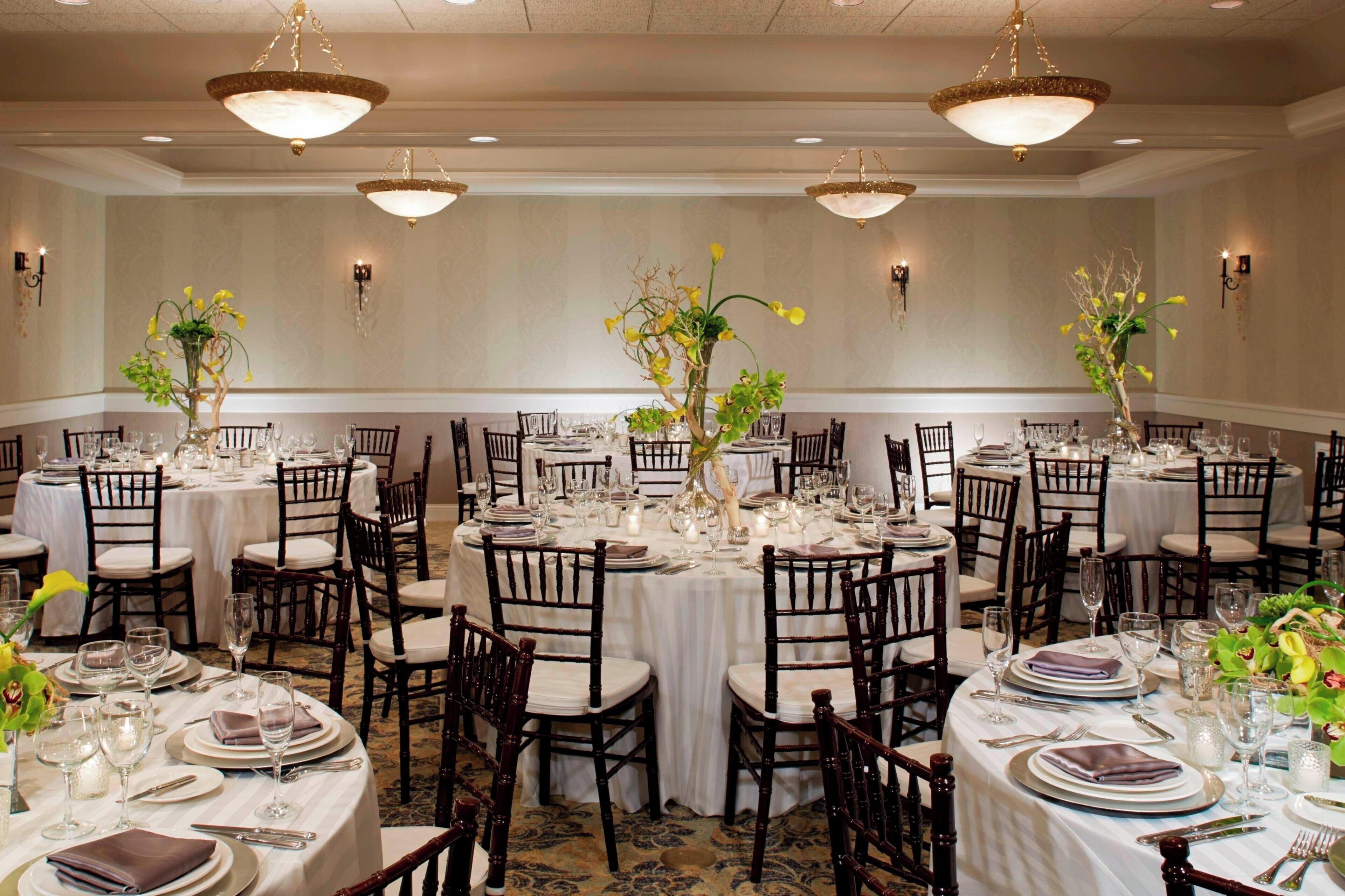 A banquet hall with round tables, dark wooden chairs, and white tablecloths.