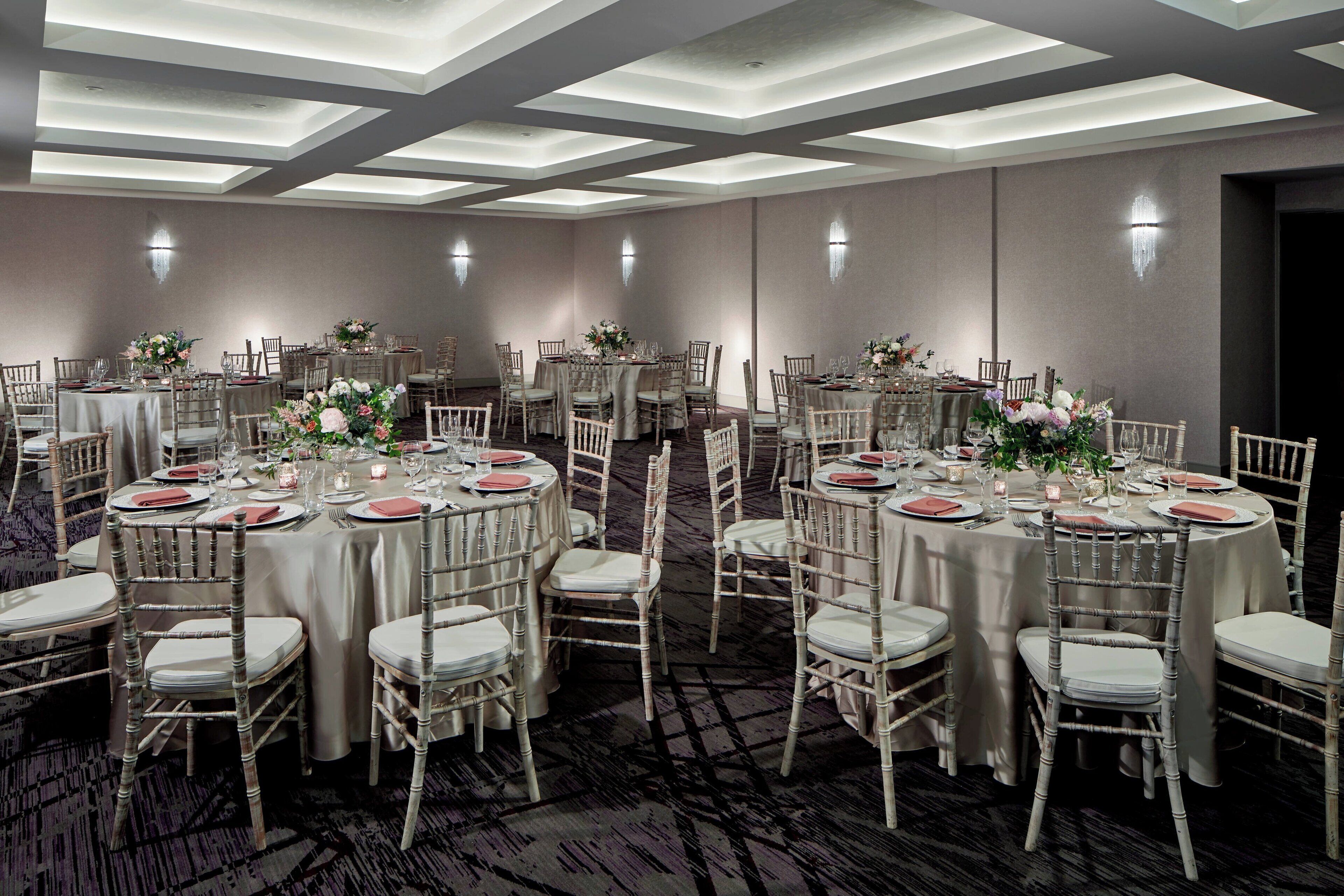 A banquet hall with round tables, white chairs, and floral centerpieces.