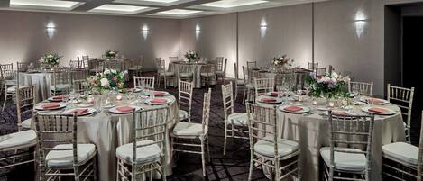 A banquet hall with round tables, white chairs, and floral centerpieces.