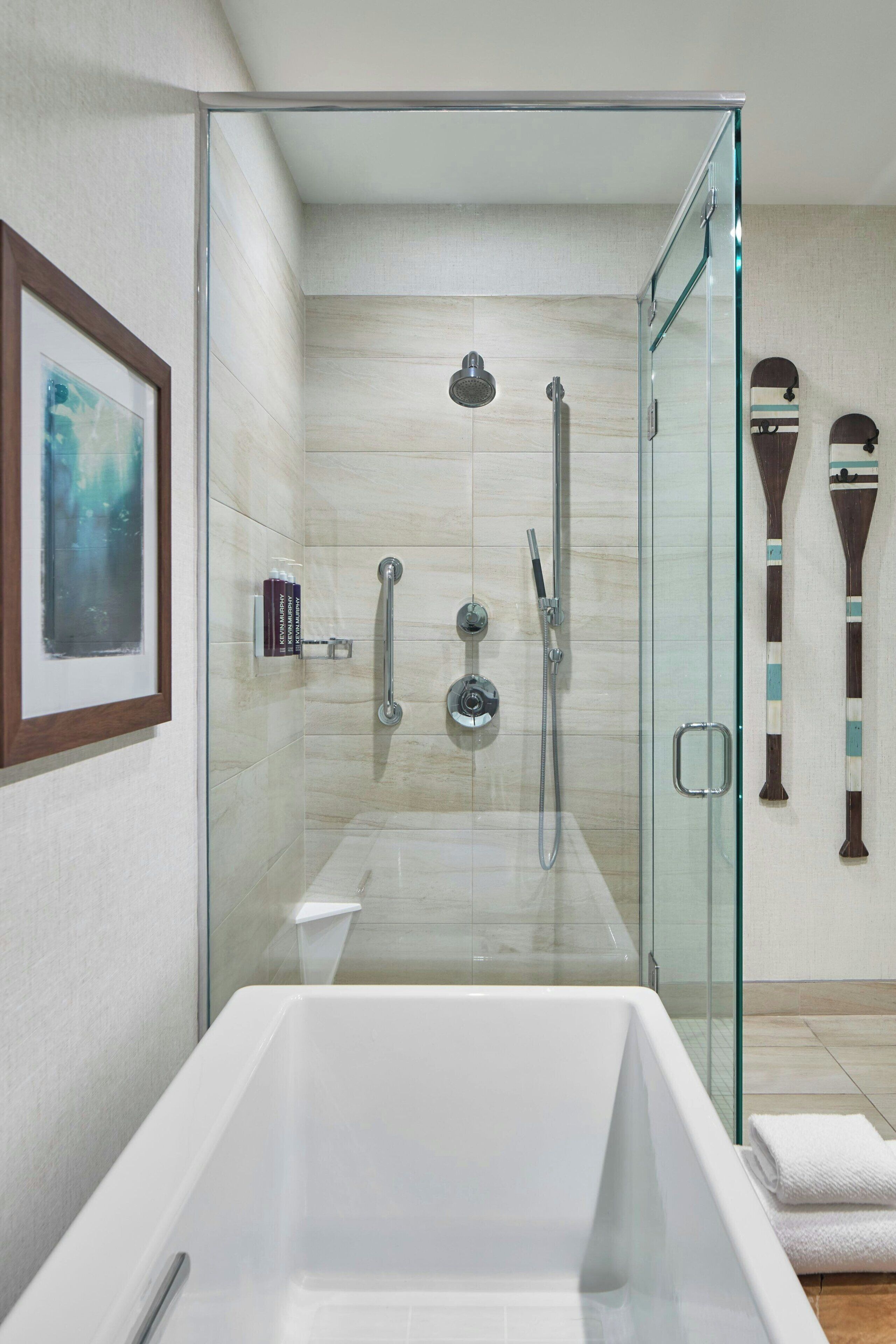 Een moderne badkamer met een douchecabine van glas, een witte badkuip en een ingelijste afbeelding aan de muur.