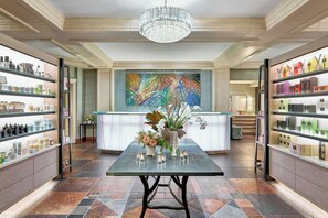 A spacious lobby with a central table, surrounded by shelves of toiletries and a large abstract painting on the wall.