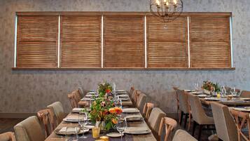 A dining area with a long table set for a meal, surrounded by chairs, with a decorative wall and a chandelier above.
