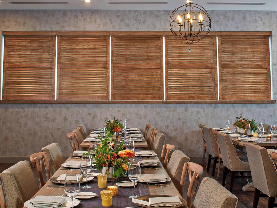 A dining area with a long table set for a meal, surrounded by chairs, with a decorative wall and a chandelier above.