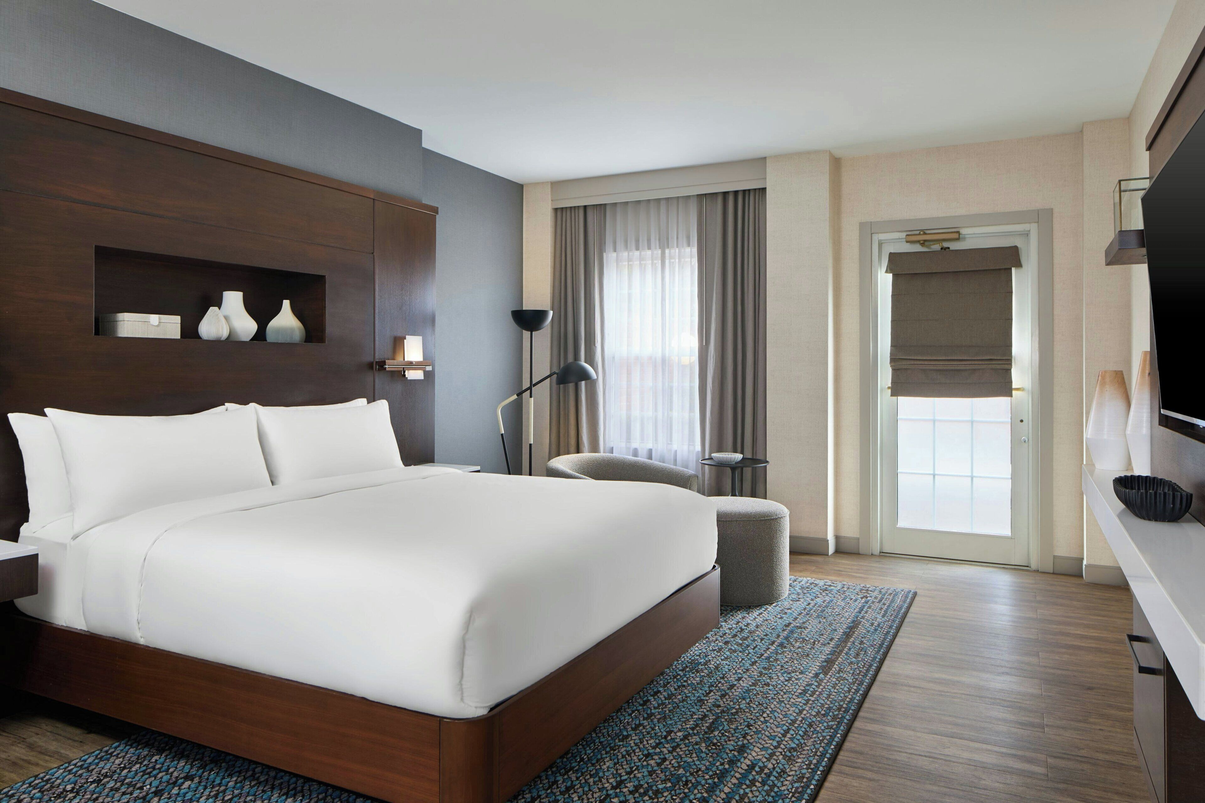 Una habitación de hotel con una cama grande, un escritorio, una silla, un televisor y una ventana con cortinas.