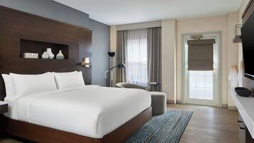 Una habitación de hotel con una cama grande, un escritorio, una silla, un televisor y una ventana con cortinas.