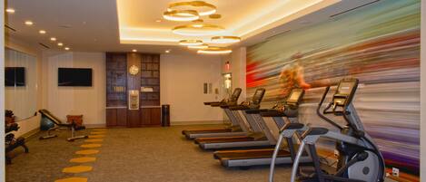 Ein Fitnessstudio mit Laufbändern, Ergometer und einer Wand mit einem verschwommenen Bewegungseffekt.