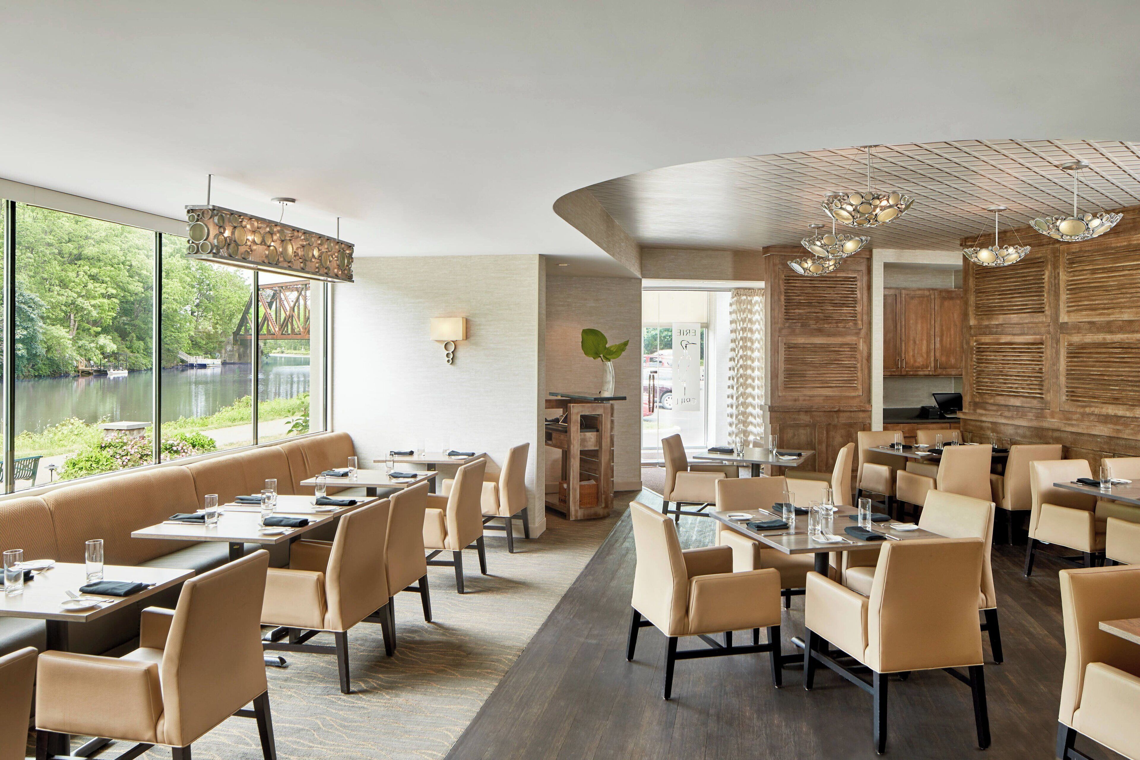 Un restaurante moderno con vistas a un lago, que ofrece mesas altas y cabinas, paneles de madera e iluminación contemporánea.