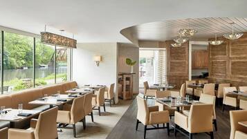 Un restaurante moderno con vistas a un lago, que ofrece mesas altas y cabinas, paneles de madera e iluminación contemporánea.