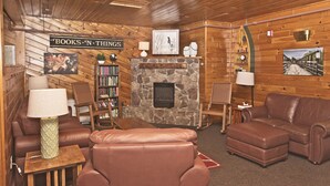 A cozy log cabin interior with a stone fireplace, leather sofas, a bookshelf, and a 'Books N Things' sign. - River View Resort (Bethel)