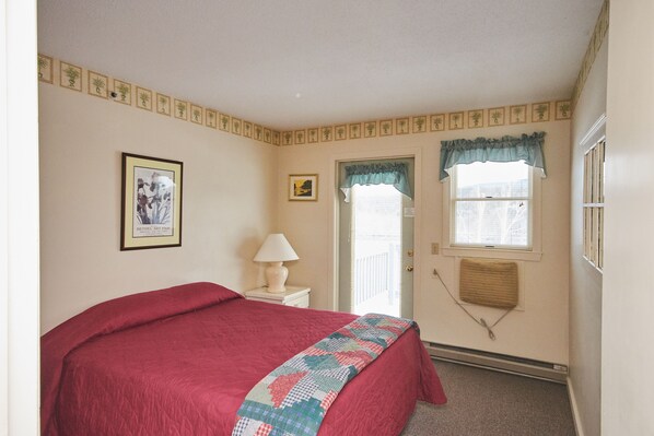 A bedroom with a bed, a nightstand, a lamp, a window with a valance, and a door.