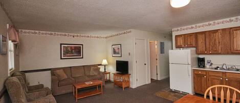A compact living space with a sofa, armchairs, a coffee table, a television, a dining table, and wooden cabinets.