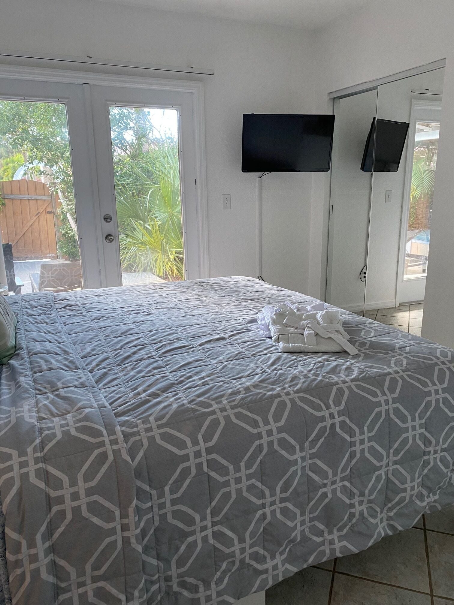 Un dormitorio con cama, televisor en la pared y puerta que da a un balcón.