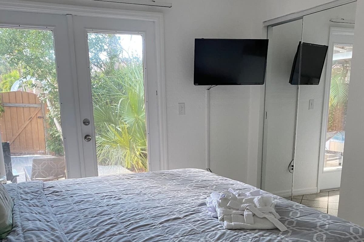 A bedroom with a bed, a TV mounted on the wall, and a door leading to a balcony.
