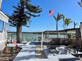 Una terraza con mobiliario exterior, vista a un cuerpo de agua y una bandera.