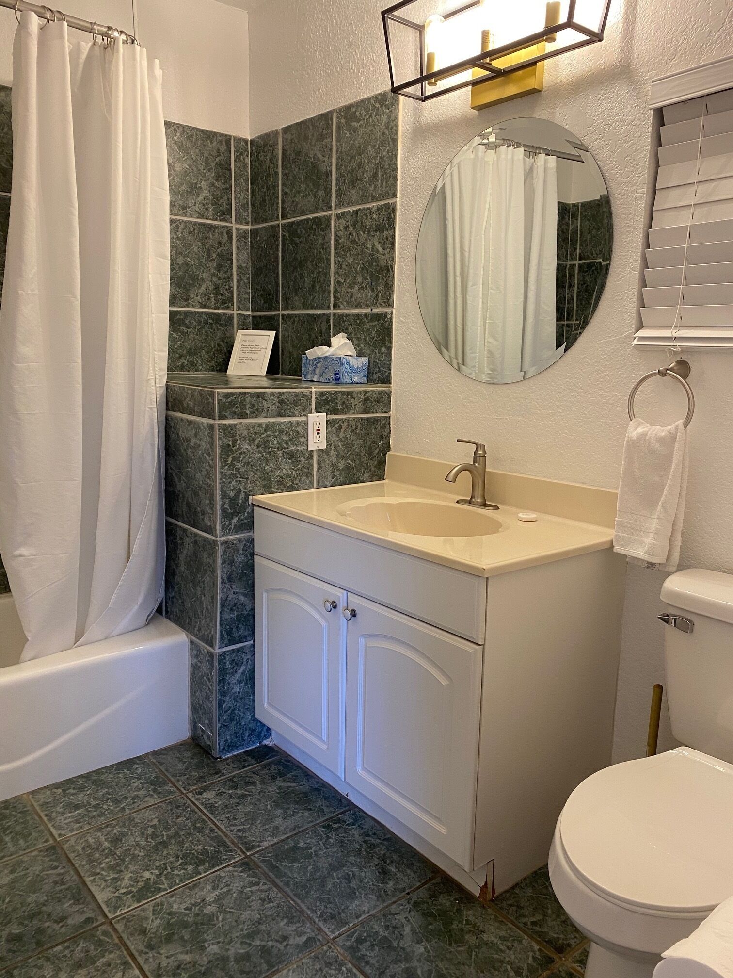 Un baño con bañera, lavamanos con espejo, inodoro y azulejos de mármol verde.