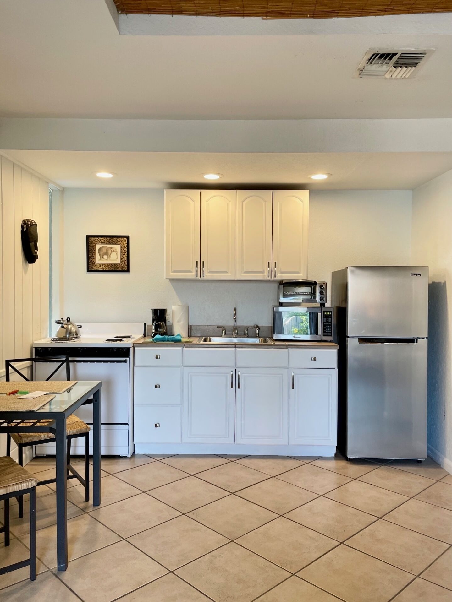 A compact kitchen with white cabinets, a stainless steel refrigerator, a microwave, and a small dining area with a table and chairs.
