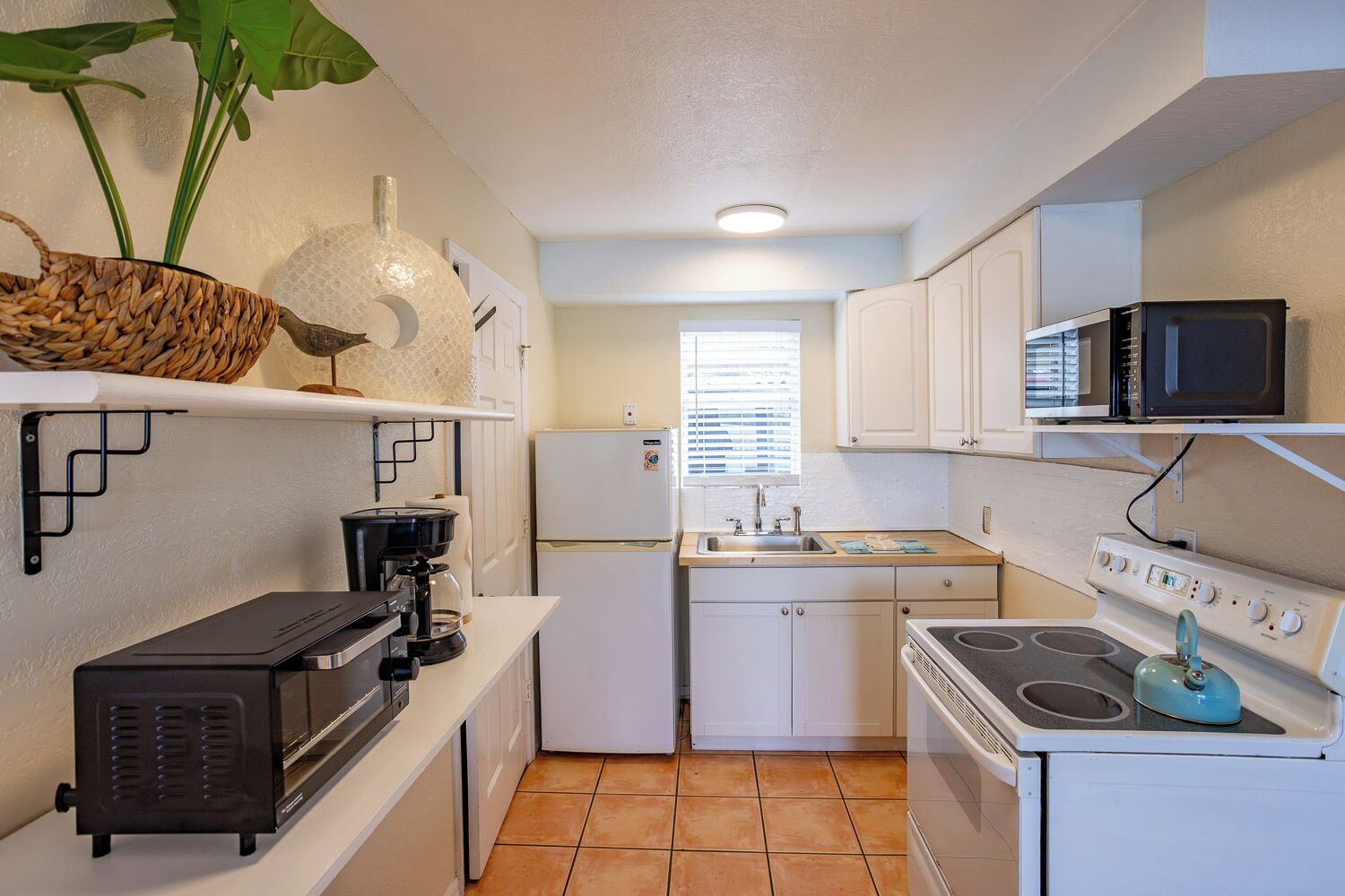 A compact kitchen with a refrigerator, microwave, stove, and coffee maker.