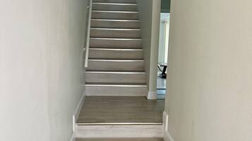 A staircase with wooden steps and white trim, leading to a room with a bed and a lamp.