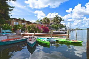A marina with several boats docked, a wooden dock, and a house with a garden in the background.