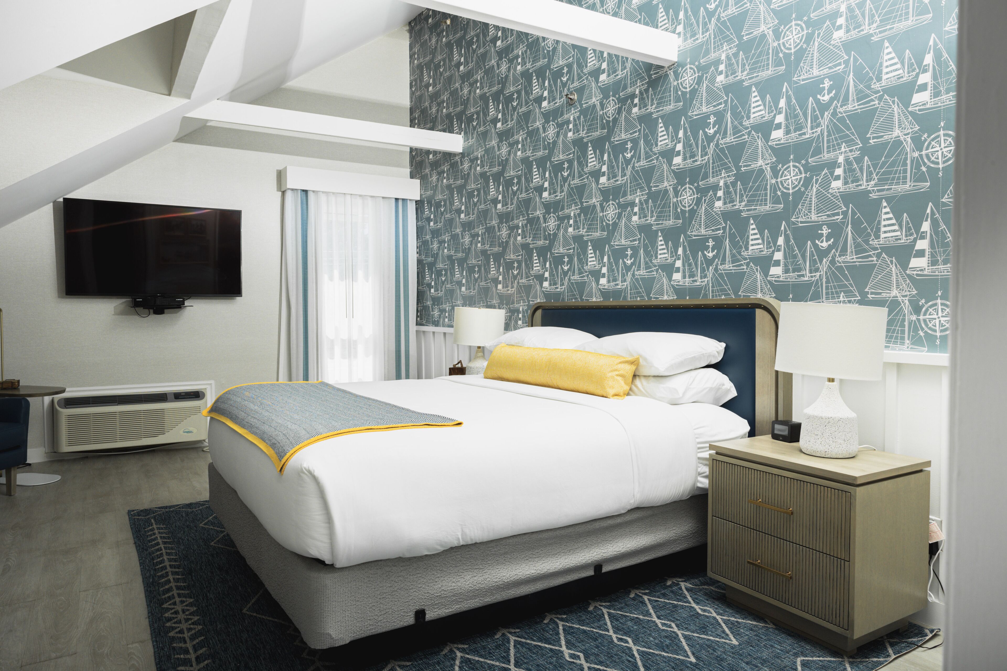 A hotel room with a bed, a nightstand, a TV, and a patterned wall.
