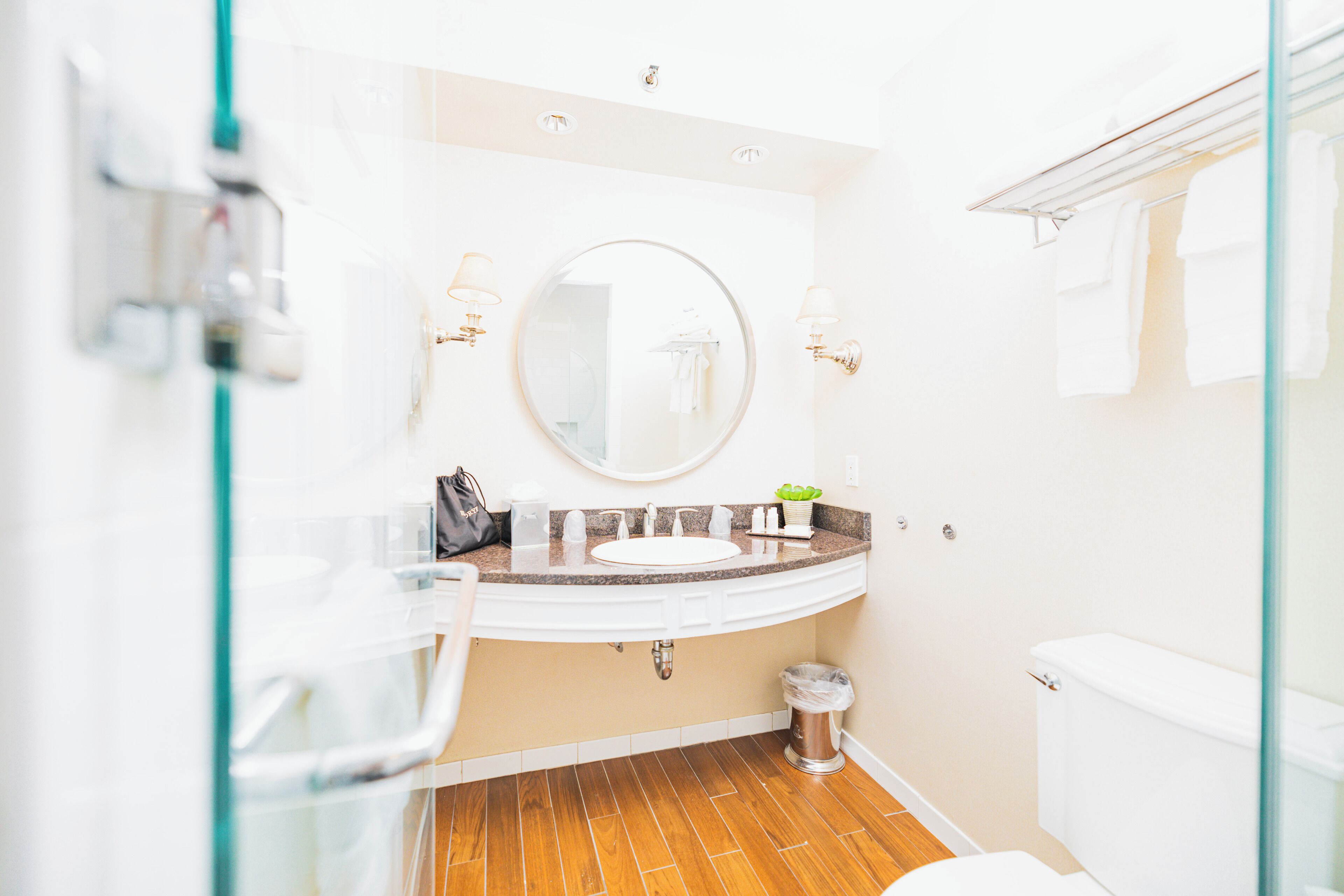 A bathroom with a white sink, round mirror, and wooden flooring.