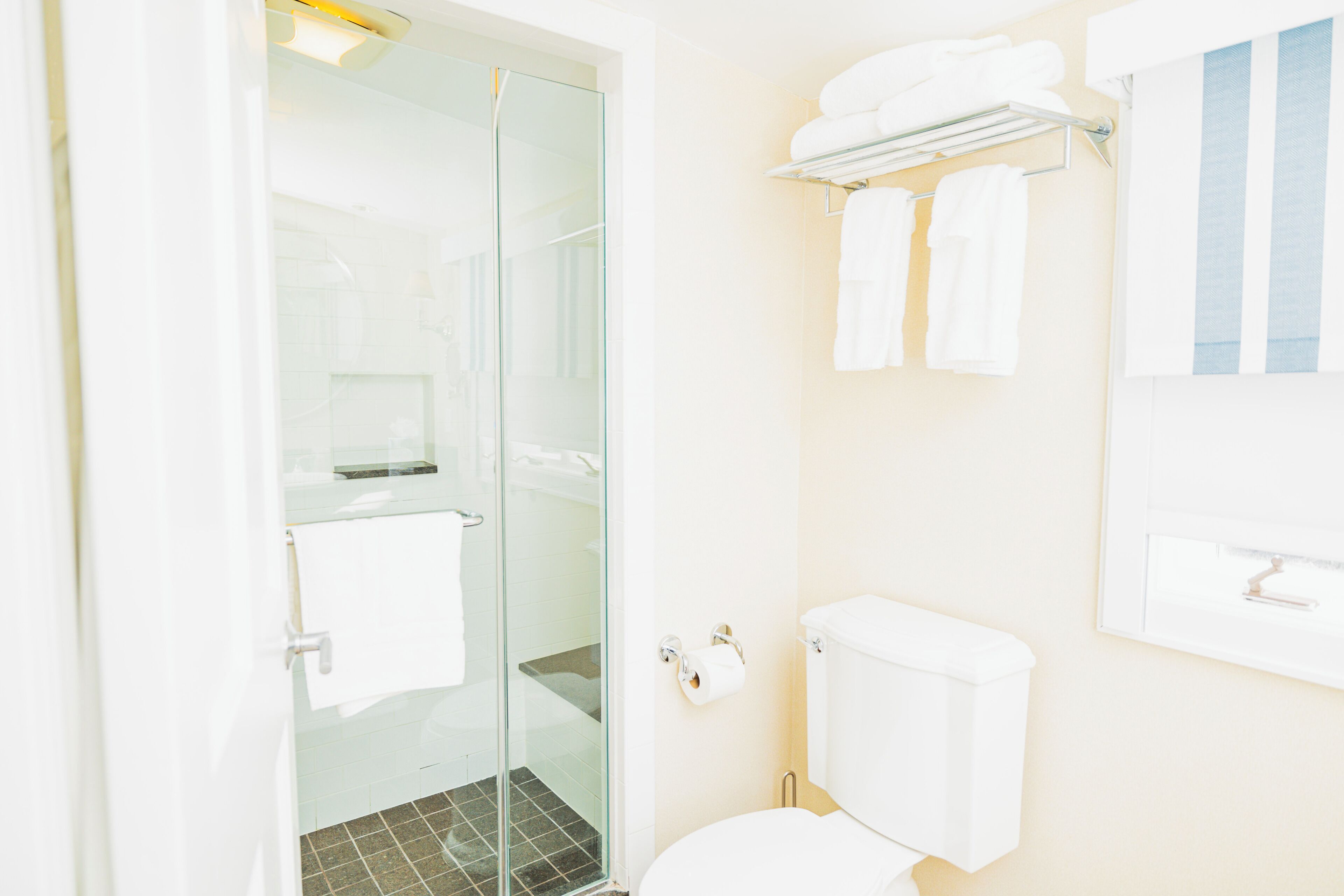 A modern bathroom with a glass shower enclosure, a toilet, and a towel rack with folded towels.