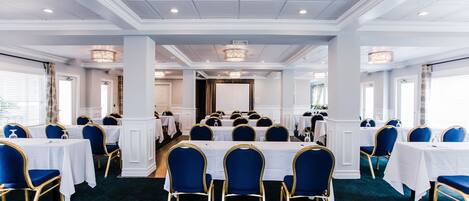 A formal dining room with round tables, blue upholstered chairs, and a chandelier.